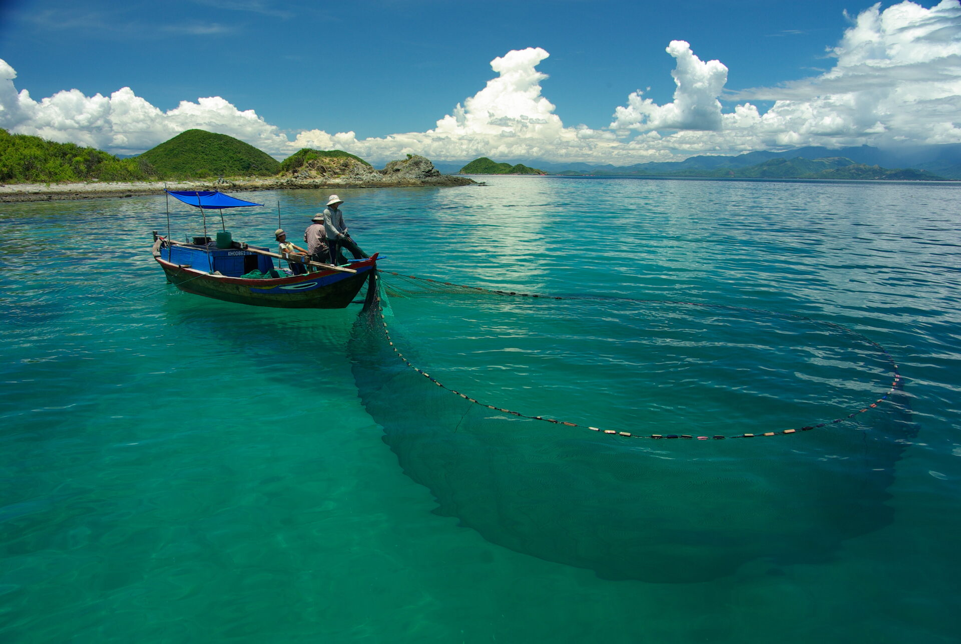 A small fishing boat and fishermen fish using a net.