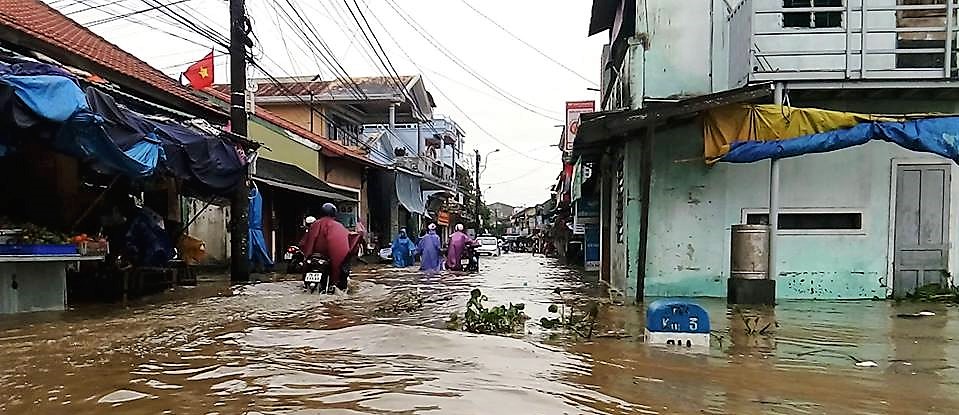 Flooded road in Vietnam with people trying to get through the flood on motorbikes. The water is above their knees.