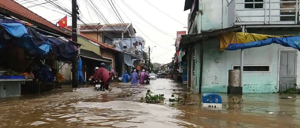 Flooded road in Vietnam with people trying to get through on motorbikes.
