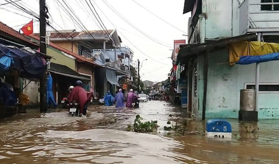 Flooded road in Vietnam with people trying to get through on motorbikes.