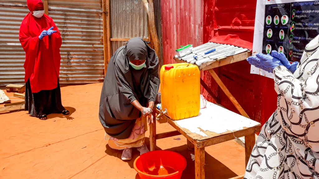 Women with a mask on filling up water from a jug.