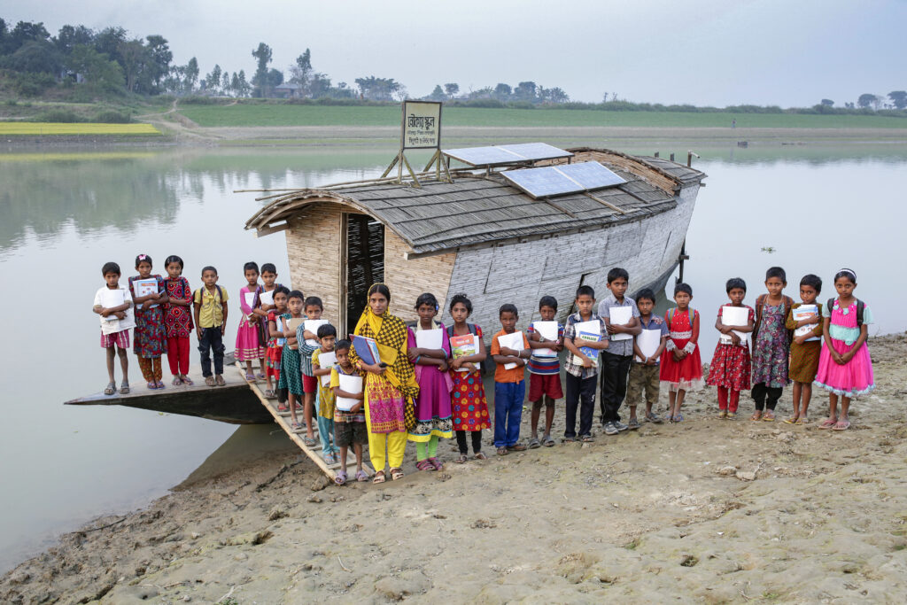 Students and their teacher stand outside a boat school in Bangladesh