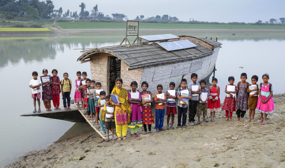 Students and their teacher stand outside a boat school in Bangladesh